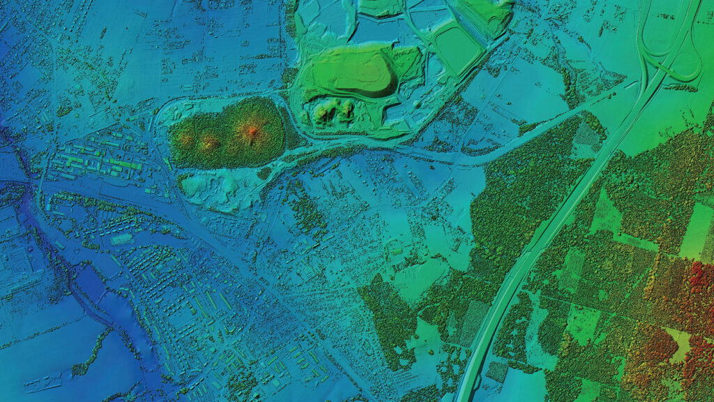A topographic map in shades of blue, green, and yellow highlights roads, urban structures, and landforms. Elevation changes are marked by color shifts, with higher areas in yellow and lower in blue. Distinguishable forested and open areas enhance the detail offered by expert Land Survey Services.