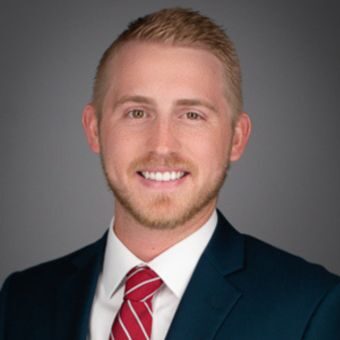 Jake Pharis, Vice President of Finance A smiling man with short light hair and a beard, dressed in a dark suit, white shirt, and red striped tie, exudes professionalism akin to that required in land surveying. The background is plain gray.